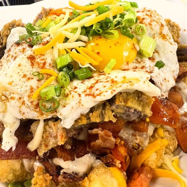 A fried egg with cheddar and scallions over a loaded breakfast plate